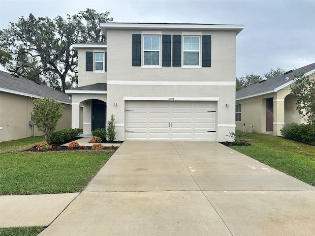 traditional-style house with a garage, driveway, a front yard, and stucco siding