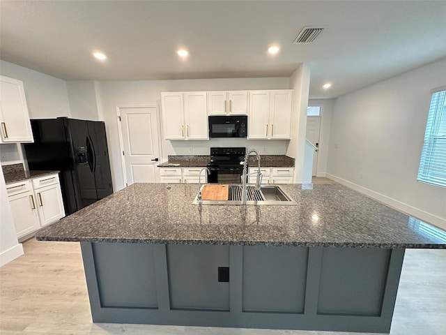 kitchen featuring a large island with sink, white cabinets, a sink, and black appliances