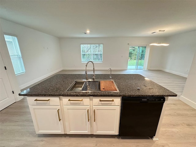 kitchen featuring light wood-style flooring, a sink, black dishwasher, dark stone counters, and an island with sink