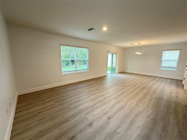 empty room with an inviting chandelier, wood finished floors, visible vents, and baseboards