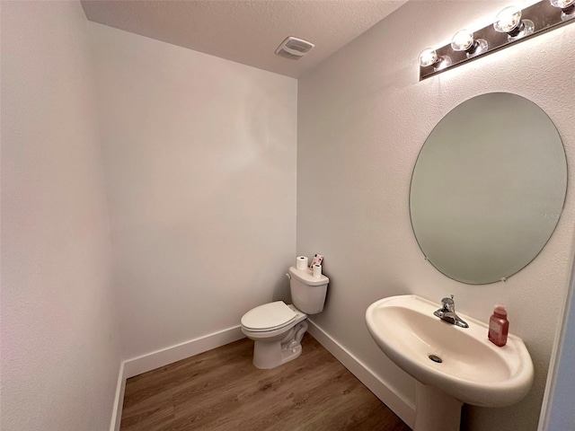 half bathroom featuring toilet, wood finished floors, a sink, visible vents, and baseboards