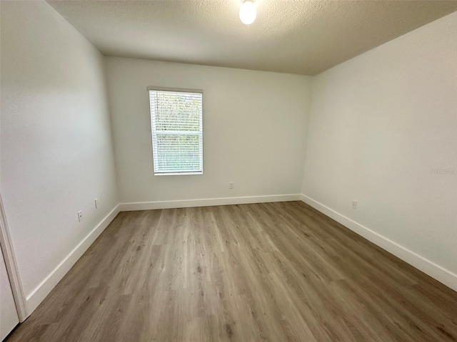 spare room featuring a textured ceiling, wood finished floors, and baseboards