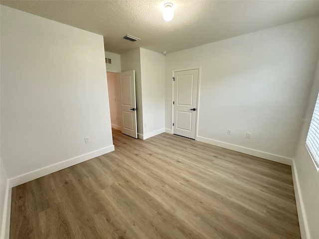 unfurnished bedroom featuring visible vents, a textured ceiling, baseboards, and wood finished floors