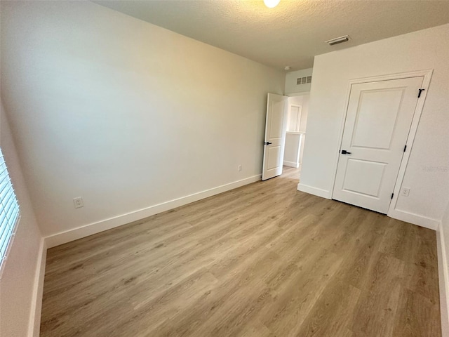 unfurnished bedroom featuring light wood-style floors, visible vents, a textured ceiling, and baseboards