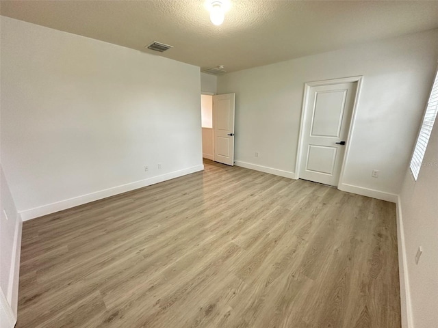 unfurnished bedroom with light wood-style floors, baseboards, visible vents, and a textured ceiling