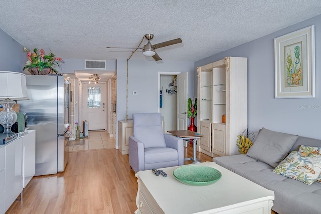 living room featuring a ceiling fan, light wood-style flooring, visible vents, and a textured ceiling