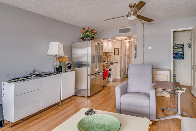 living area with light wood-style floors, visible vents, a textured ceiling, and a ceiling fan