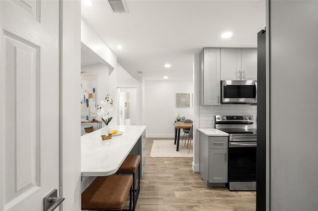 kitchen featuring light wood-style flooring, gray cabinets, stainless steel appliances, backsplash, and recessed lighting