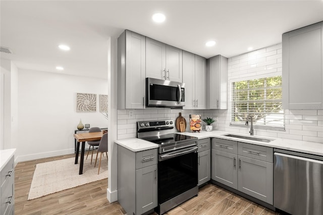 kitchen featuring stainless steel appliances, a sink, decorative backsplash, and gray cabinetry