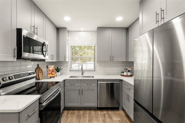 kitchen with stainless steel appliances, gray cabinets, backsplash, light wood-style floors, and a sink