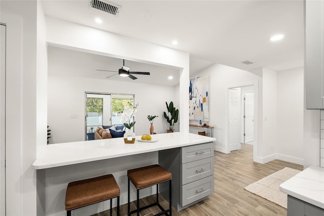 kitchen featuring visible vents, light stone counters, gray cabinetry, light wood-style floors, and a kitchen bar