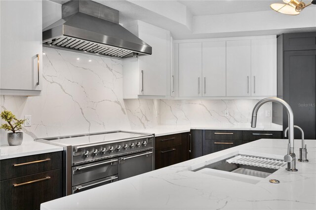 kitchen with decorative backsplash, white cabinets, wall chimney exhaust hood, double oven range, and a sink