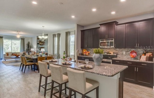 kitchen with decorative backsplash, appliances with stainless steel finishes, an island with sink, light stone countertops, and a kitchen bar