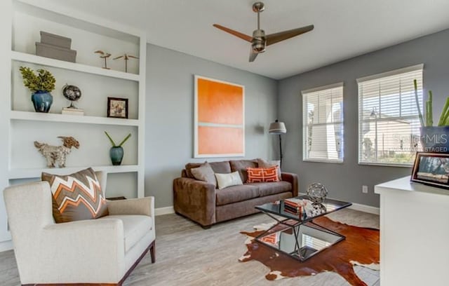 living room featuring built in features, a ceiling fan, baseboards, and wood finished floors