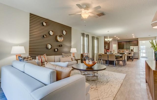 living room with ceiling fan with notable chandelier, light wood-style flooring, and visible vents