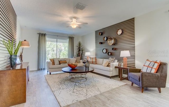 living room featuring a textured ceiling, ceiling fan, wood finished floors, visible vents, and baseboards