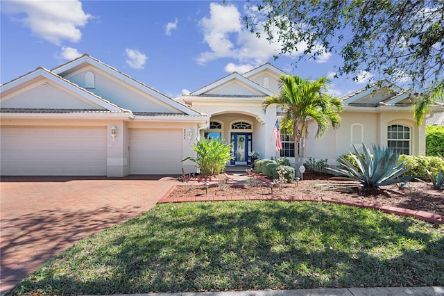 view of front of property featuring decorative driveway, a front yard, an attached garage, and stucco siding