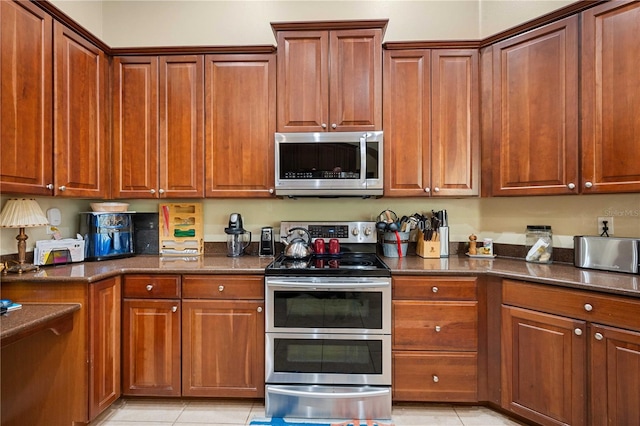 kitchen with dark stone countertops, light tile patterned floors, brown cabinets, and stainless steel appliances