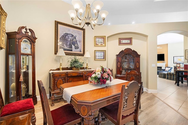 dining space with baseboards, a chandelier, light wood-type flooring, a fireplace, and arched walkways