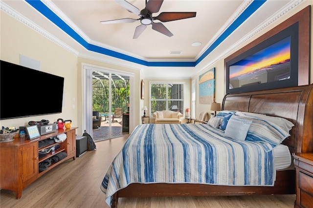 bedroom with visible vents, ornamental molding, wood finished floors, a raised ceiling, and access to outside