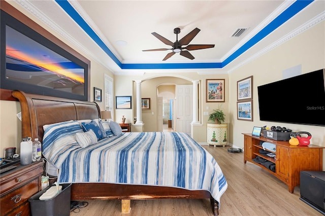 bedroom with a raised ceiling, decorative columns, wood finished floors, and ornamental molding