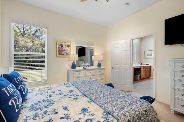 bedroom with connected bathroom, multiple windows, light colored carpet, and baseboards