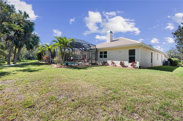 rear view of property featuring a lanai, a lawn, cooling unit, a chimney, and stucco siding