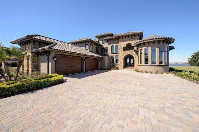 mediterranean / spanish-style home featuring stone siding, stucco siding, an attached garage, and decorative driveway