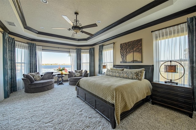 bedroom with a water view, ornamental molding, a tray ceiling, a textured ceiling, and carpet flooring