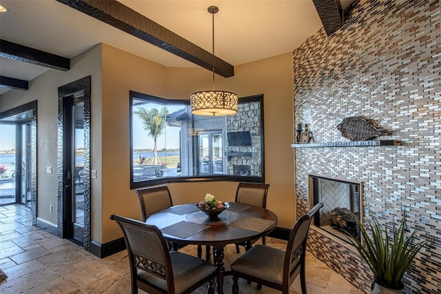 dining space featuring baseboards, beam ceiling, stone tile floors, and a tile fireplace