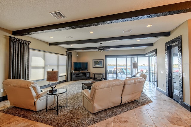 living room featuring stone tile flooring, visible vents, beam ceiling, and baseboards