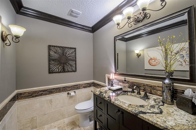 half bath featuring crown molding, toilet, vanity, a textured ceiling, and tile walls