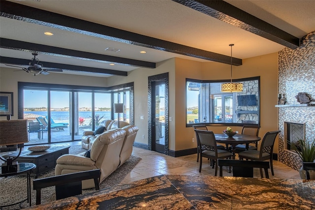 living room with a water view, beam ceiling, a ceiling fan, baseboards, and a tile fireplace