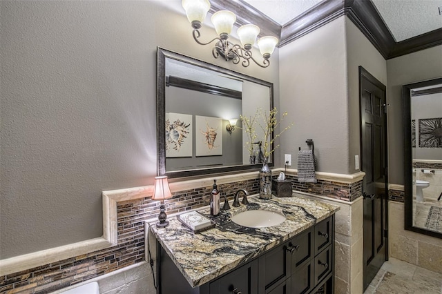 bathroom with stone tile floors, vanity, a textured wall, and ornamental molding