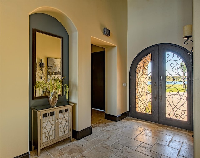 entrance foyer with baseboards, french doors, arched walkways, and stone tile floors