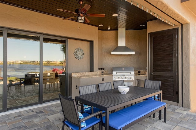 view of patio featuring grilling area, a water view, outdoor dining area, an outdoor kitchen, and a ceiling fan