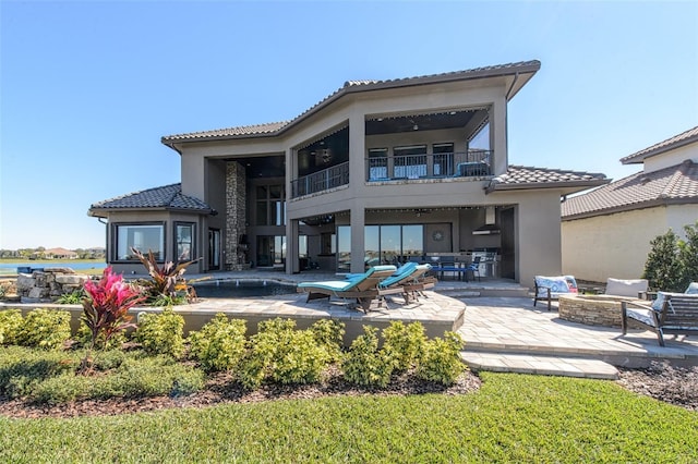 back of house featuring stucco siding, a tile roof, a patio, an outdoor living space with a fire pit, and a balcony