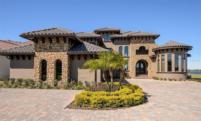 mediterranean / spanish-style home featuring decorative driveway, stone siding, and stucco siding