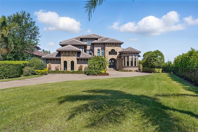 mediterranean / spanish-style home with a tiled roof, stone siding, fence, a front yard, and stucco siding