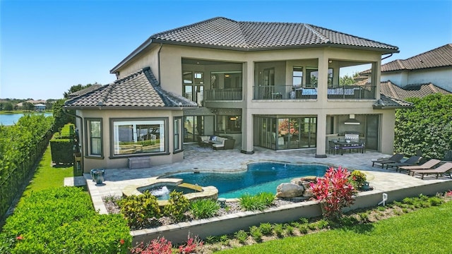 rear view of house featuring a tiled roof, a patio area, a balcony, a pool with connected hot tub, and stucco siding