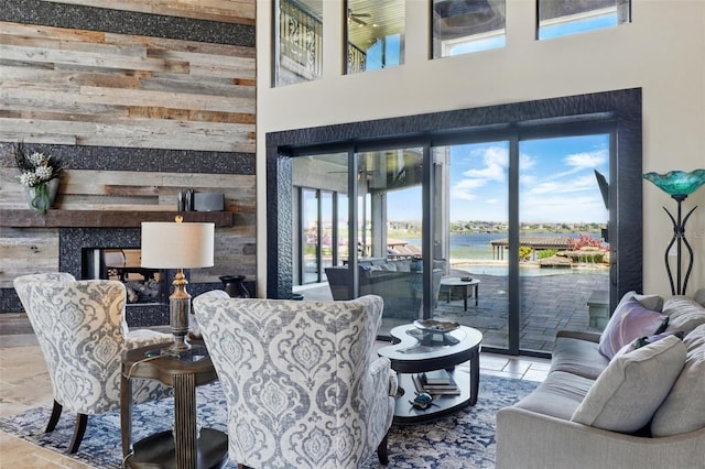 living room featuring a fireplace, wood walls, a towering ceiling, and a water view