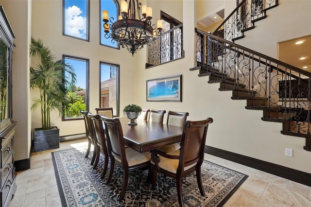 dining space with stairway, a towering ceiling, stone tile flooring, baseboards, and a notable chandelier