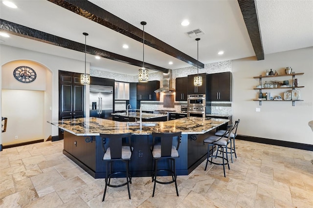 kitchen with a large island, stone tile flooring, stainless steel appliances, and beamed ceiling
