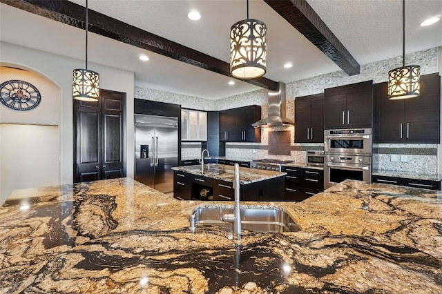 kitchen featuring stainless steel appliances, backsplash, wall chimney range hood, a sink, and beam ceiling