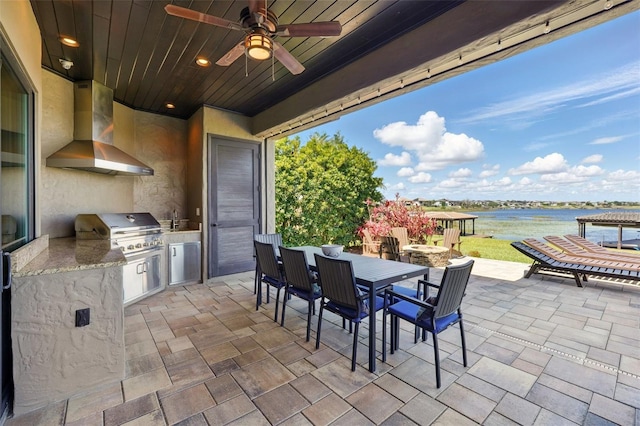 view of patio / terrace featuring a water view, outdoor dining space, a ceiling fan, a grill, and exterior kitchen