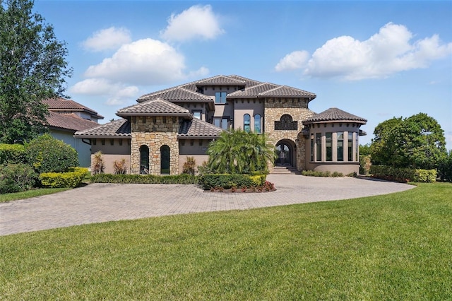 mediterranean / spanish-style house featuring a tile roof, stone siding, a front lawn, and stucco siding