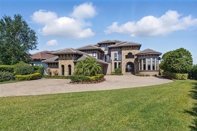 mediterranean / spanish-style house featuring stucco siding, a tile roof, decorative driveway, stone siding, and a front yard