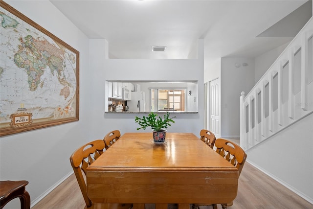 dining space featuring light wood-style floors, visible vents, stairway, and baseboards