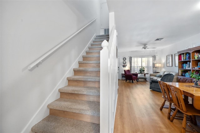 staircase featuring wood finished floors, visible vents, and a ceiling fan