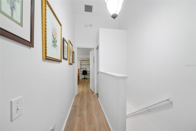 hallway with baseboards, an upstairs landing, visible vents, and light wood-style floors